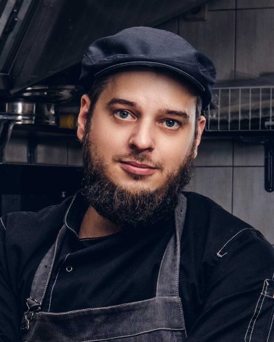 bearded-cook-in-black-uniform-and-hat-holds-knife-BMEASJV.jpg